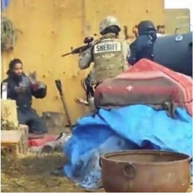 Militarized police point a gun at a Standing Rock water protector to shut down the camp.