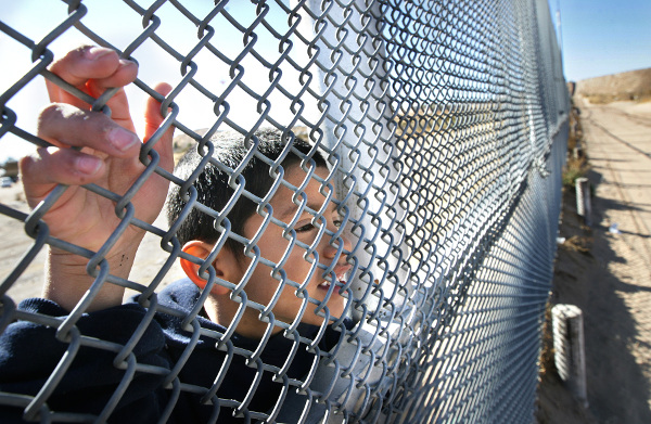 Young Mexican boy watches Border Patrol on New Mexico side of border fence