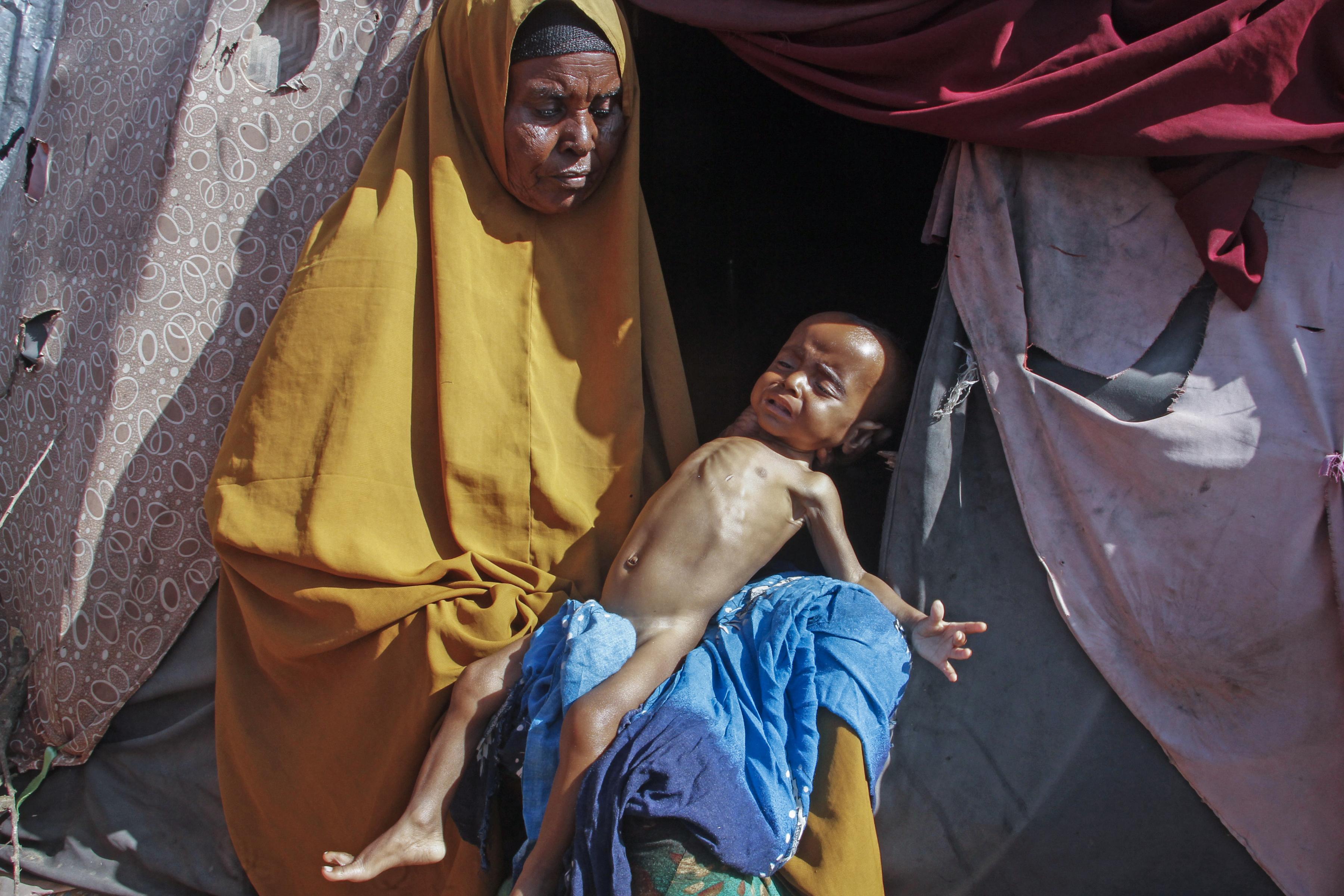 63-year-old with grandchild outside tent camp, after fleeing drought in Somalia.