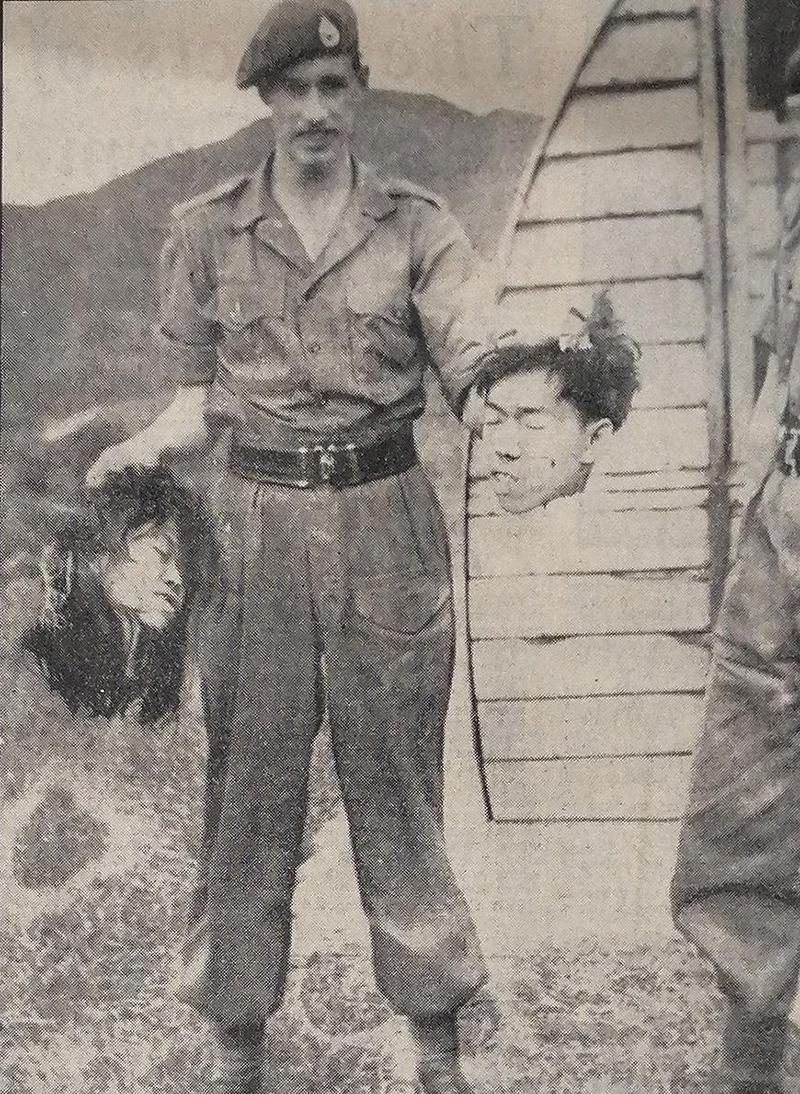 British soldier poses with decapitated heads of Malayans