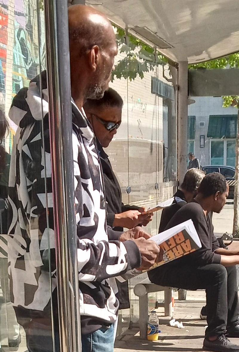 Guys at bus stop in Chicago read We Are the Revcoms.