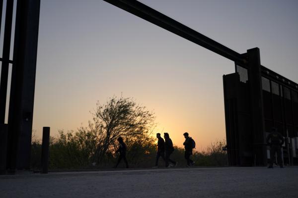 People waiting to cross border silhouetted against sky at gap in border wall Texas