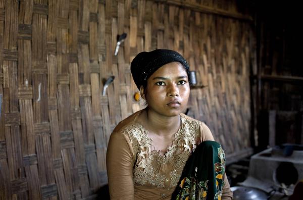 Rohingya woman who escaped trafficking sits on a bed