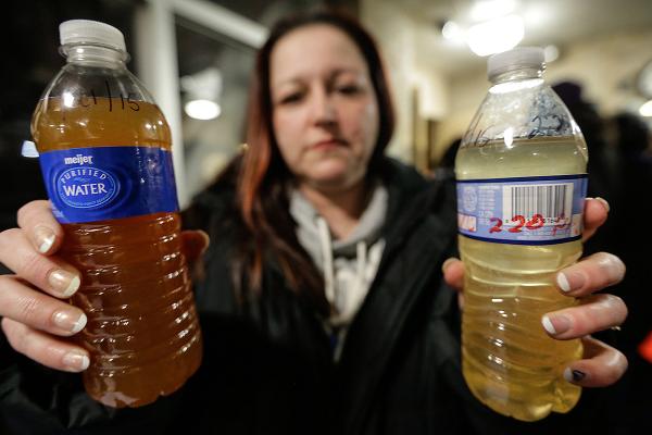 Woman holds two bottles of contaminated Flint water.