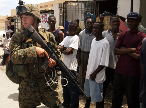 U.S. Marine walks past residents while on patrol on the outskirts of the Cite Soleil district in Port-au-Prince, Haiti. March 22, 2004.