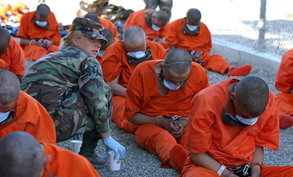 Prisoners in orange jumpsuits emprisoned in Guantanamo Bay, Camp X-ray.