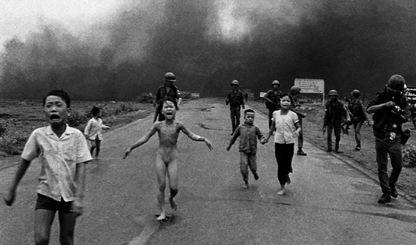 People severely burned from napalm attack run down the road.