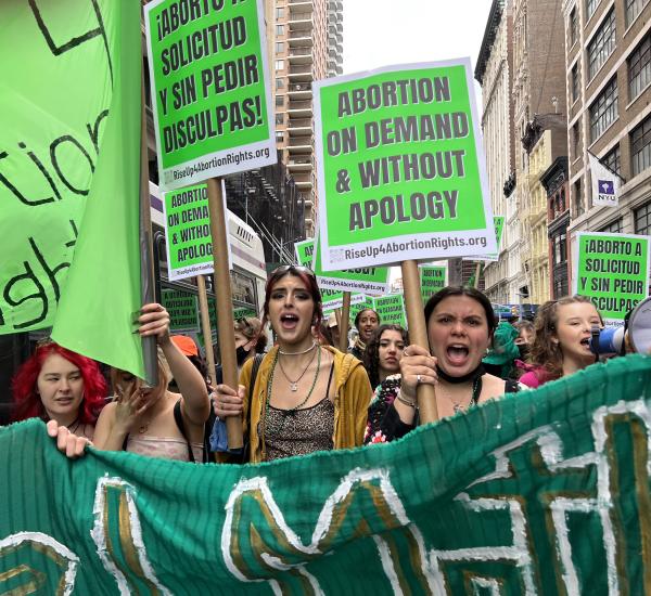 Young women march behind green banner