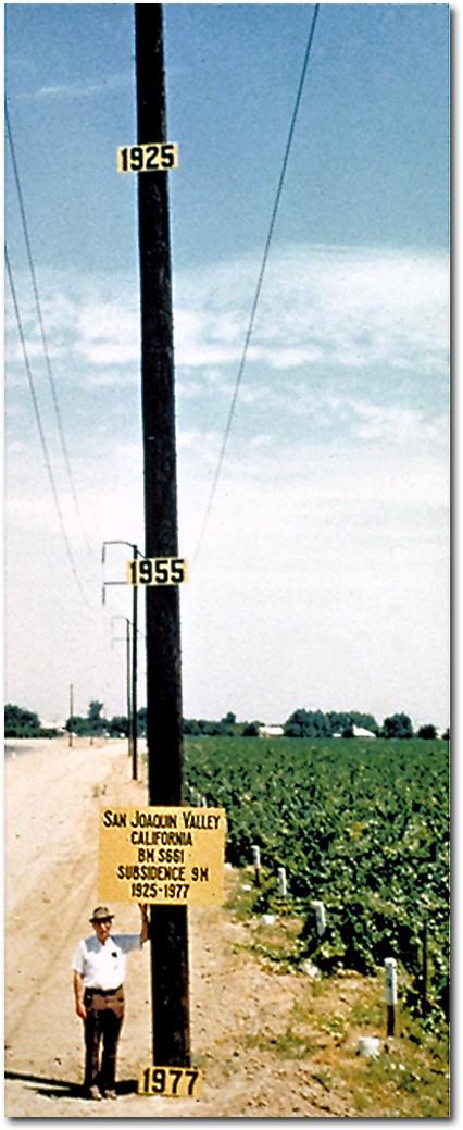 California land subsidence: Man by pole that shows markers for the level of land in years 1925, 1955 and 1977.