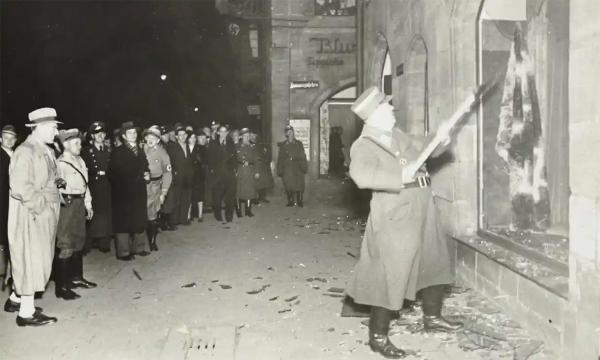 Kristallnacht, 1938: German civilians watch a Nazi officer vandalize Jewish property near Nuremberg.