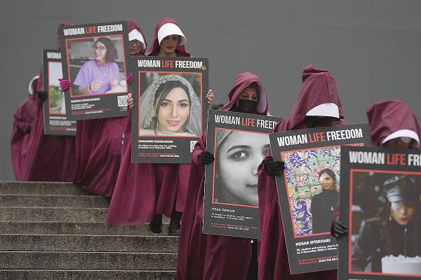 London, IWD 2023, women dressed as handmaids carry placards of Iran women killed.