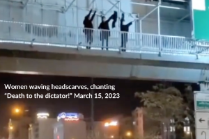 Three women on a pedestrian bridge over a highway in Tehran, waving their headscarves and chanting “Death to the dictator!” March 15, 2023 (Twitter: @1500tasvir)