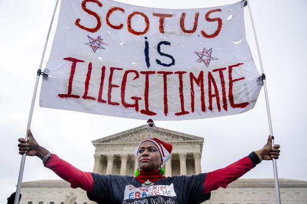 Black woman holds a banner that says SCOTUS is Illegitimate in front of the Supreme Court.
