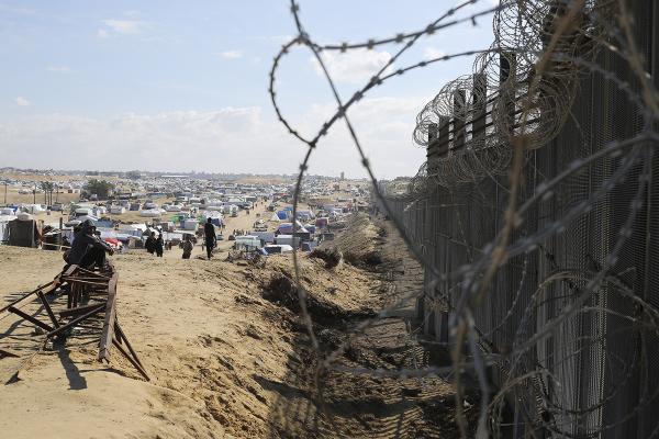 Displaced Palestinians sit next to the border fence with Egypt in Rafah, January 24, 2024. 