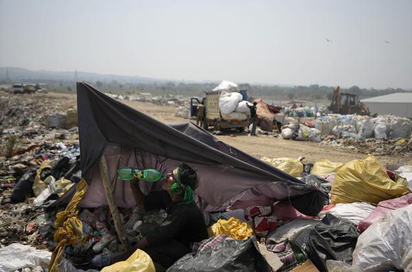  At a garbage dump on the outskirts of Jammu, India, June 19, 2024, man drinks water in the shade of trash.