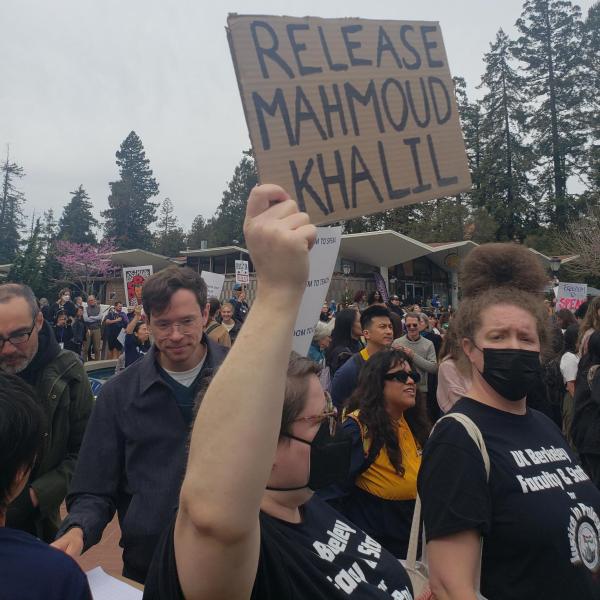 Woman with UC Berkeley shirt holds up "Release Mahmoud Khalil" sign.