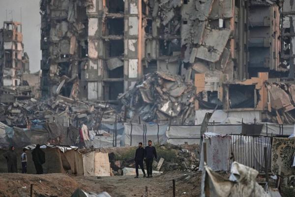 Men walk by destroyed apartment buildings at the Al-Shati camp in Gaza City, November 18, 2025.