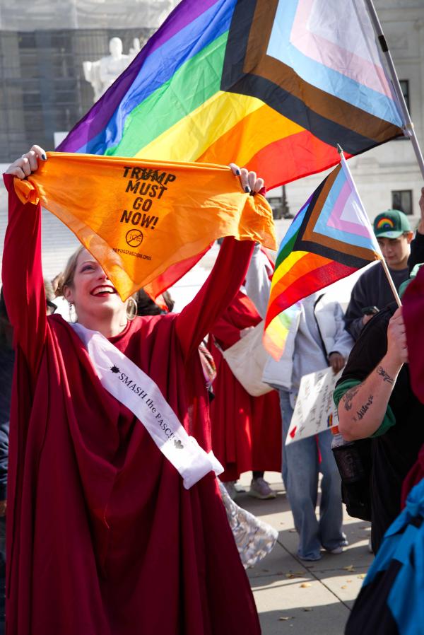 Handmaid protester displays head scarf that says Trump Must Go Now, November 7, 2025.