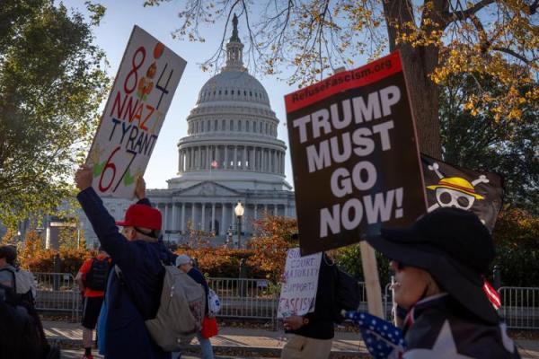 Protesters hold signs with Capitol Building in background, November 5, 2025.