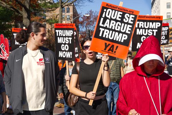 Marchers with "Trump Must Go Now" signs in Spanish in Washington DC neighborhood.