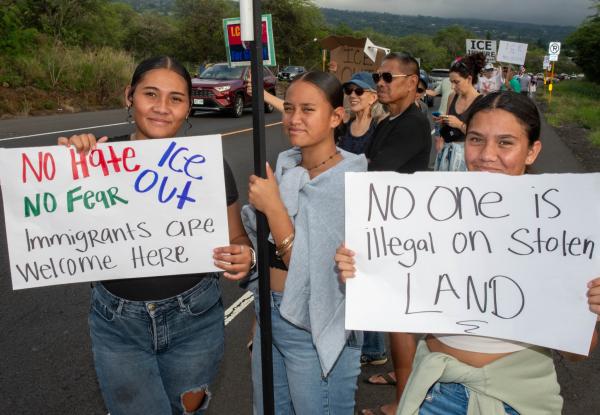 3 young women in Kona, Hawaii with sign: No One is Illegal on Stolen Land