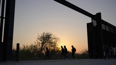 People waiting to cross border silhouetted against sky at gap in border wall Texas