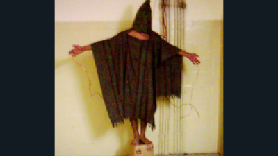 , a hooded Iraqi is shown balanced on small box, with wires attached to his fingers—he was forced to stand for hours, told that if he fell over from exhaustion, the wires would electrocute him