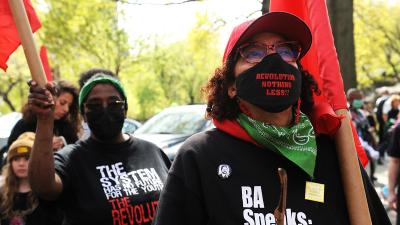 Women carrying red flags listen to speakers at New York City May Day rally.