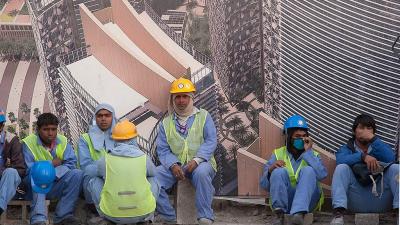 Construction workers in Qatar wait for a bus outside a construction site