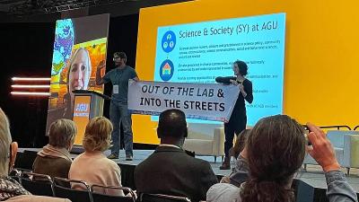 Chicago_Peter Kalmus and Rose Abramoff unfurl a banner that says "Out of the Labs and Into the Streets" during a plenary at the American Geophysical Union.