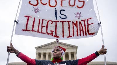 Black woman holds a banner that says SCOTUS is Illegitimate in front of the Supreme Court.