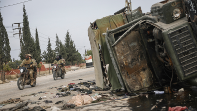 Syrian opposition fighters drive past a damaged government vehicle south of Hama, Syria, on Saturday, December 7, 2024.