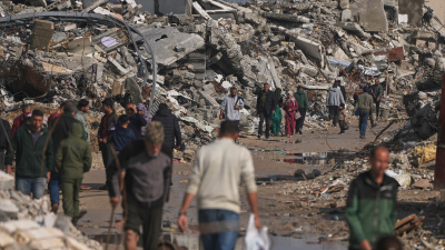 Palestinians walk along a street surrounded by buildings destroyed during Israeli air and ground operations in Gaza City, December 17, 2025.