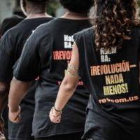 Back of woman marching with t-shirt that says ¡REVOLUCIÓN — NADA MENOS!