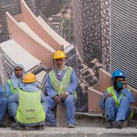 Construction workers in Qatar wait for a bus outside a construction site
