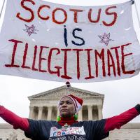 Black woman holds a banner that says SCOTUS is Illegitimate in front of the Supreme Court.