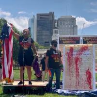 Revcoms holding the U.S. flag and red-paint-splattered constitution, July 4, in front of Independence Hall, Philadelphia.