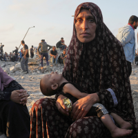 A starving Palestinian woman waits with her child for trucks with humanitarian aid to arrive in Gaza City, July 25, 2025.